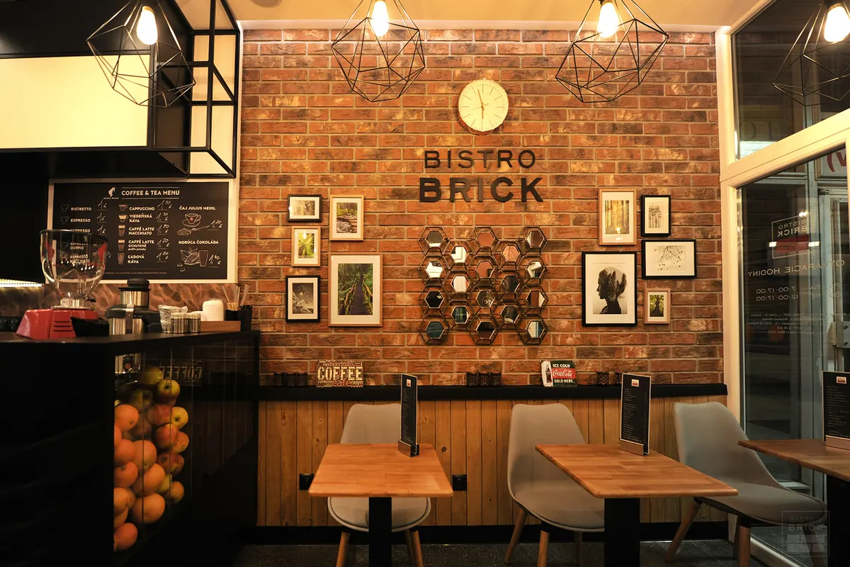 Tehlová stena s nápisom BISTRO BRICK, geometrické lustre, drevené stoly a sivé stoličky