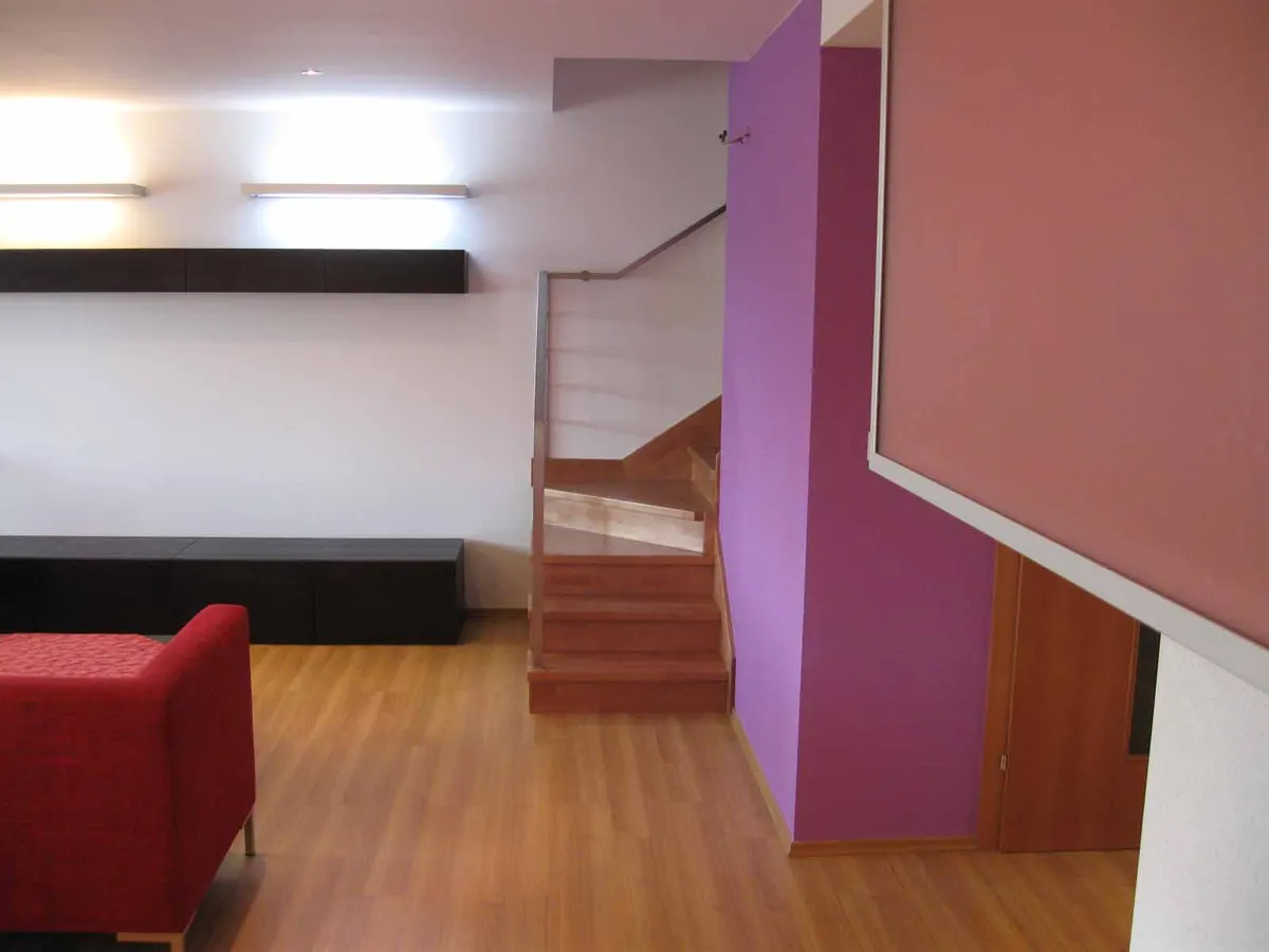 Purpurová stena, drevené schody, červené kreslo a čierny nábytok v svetlom interiéri.