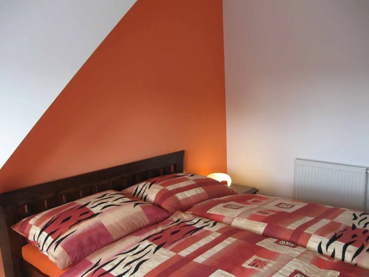 Podkrovná spálňa s oranžovou stenou, drevenou posteľou a vzorovanou bielizňou.