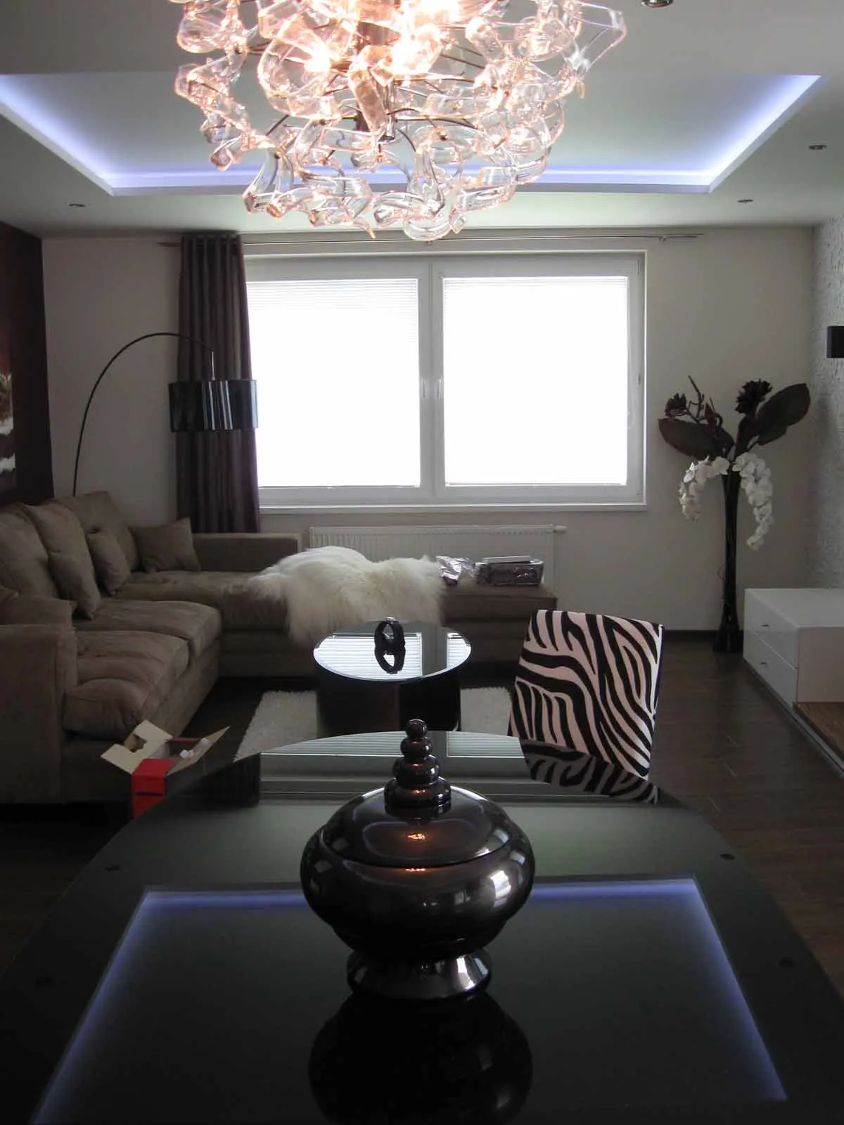 Moderná obývačka s lustrom z ružového skla, sedacou súpravou a LED osvetlením.