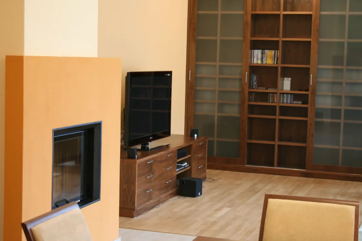 Obývacia izba s oranžovou stenou, krbovou vložkou, televízorom na drevenej skrinke a veľkou poličkou.