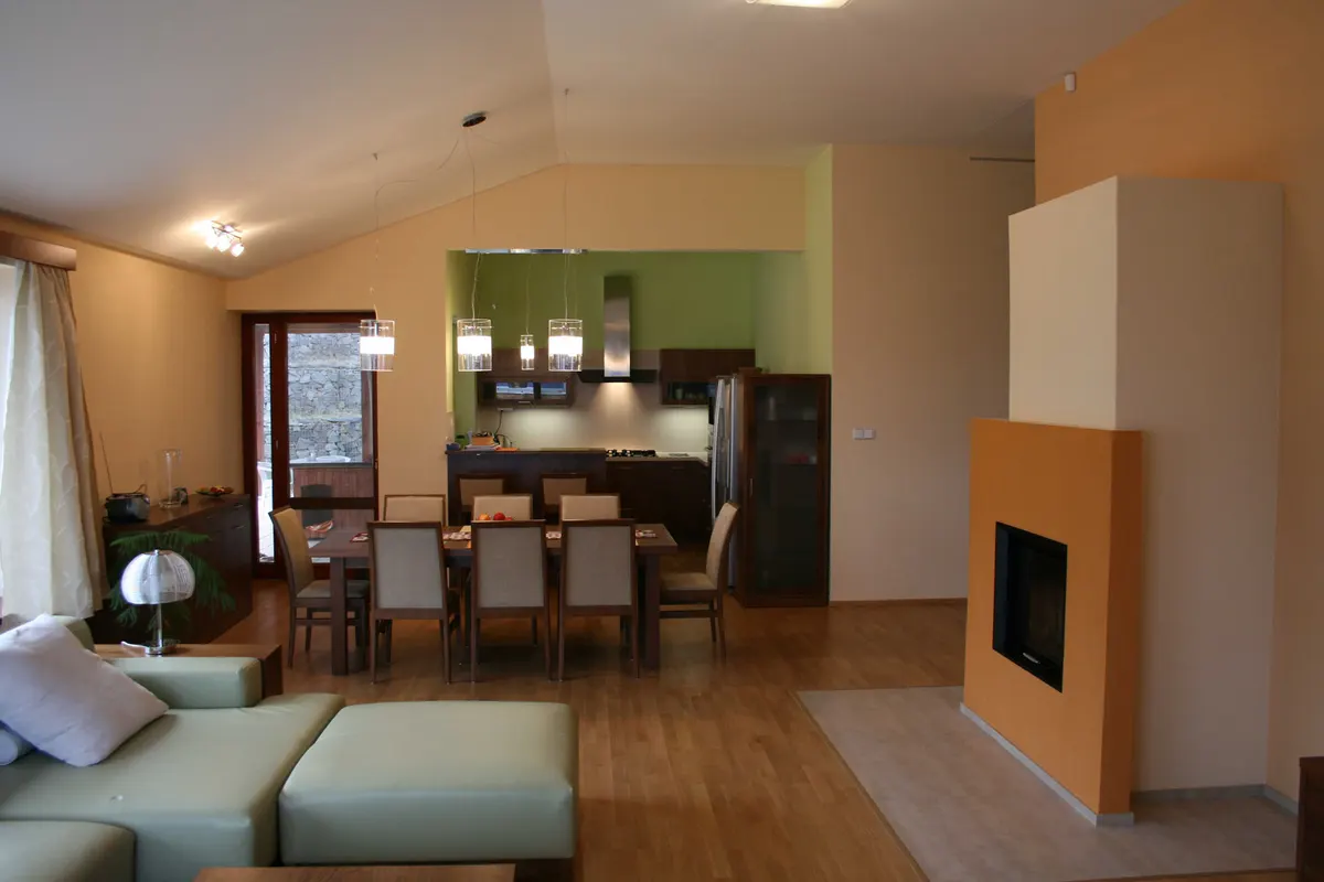 Obývačka s jedálňou a kuchyňou, oranžový krb, zelená kuchynská linka, svetlá podlaha.