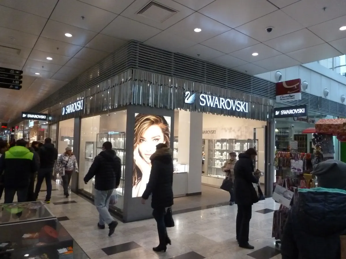Osvetlená predajňa Swarovski s presklenými vitrínami a kovovou mriežkou na fasáde.