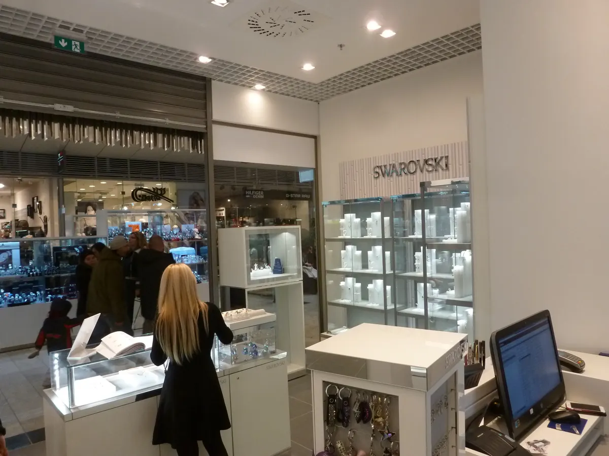Predajňa šperkov s bielymi stenami, presklenými vitrínami a nápisom SWAROVSKI.